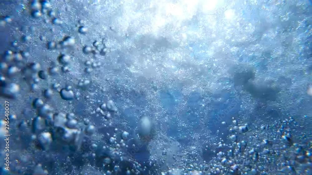 Air bubbles floating up to the water surface. Numerous small air bubbles rising up in turquoise pure sea. Warm sunshine penetrating crystal clear ocean water on sunny summer day. Slow motion Close up
