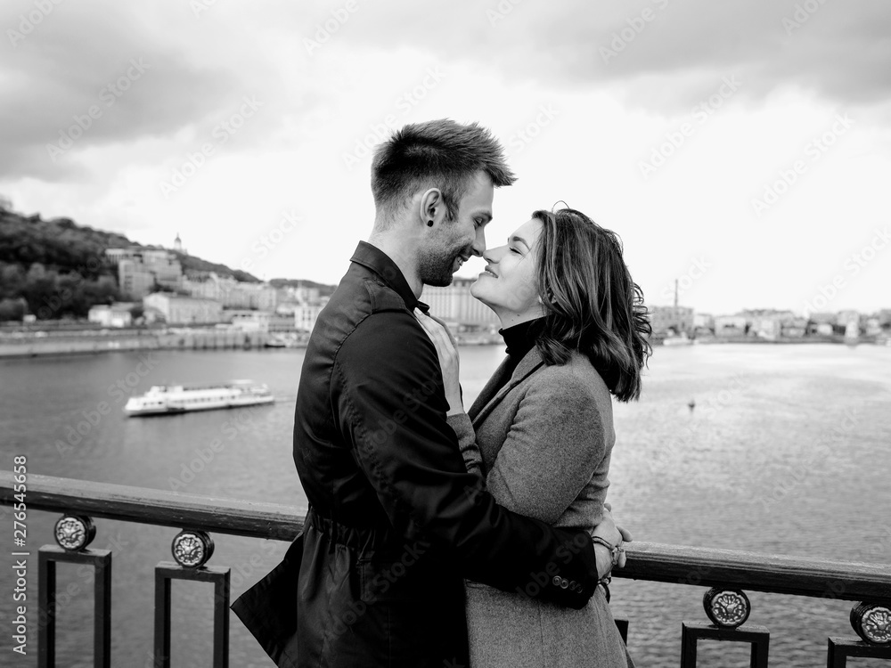 beautiful amazing sweet cheerful young couple (man and woman) standing on bridge by the river on cityscape background. Family, tenderness, dating, urban, love and friendship concept beautiful amazing sweet cheerful young couple (man and woman) standing on bridge by the river on cityscape background. Family, tenderness, dating, urban, love and friendship concept