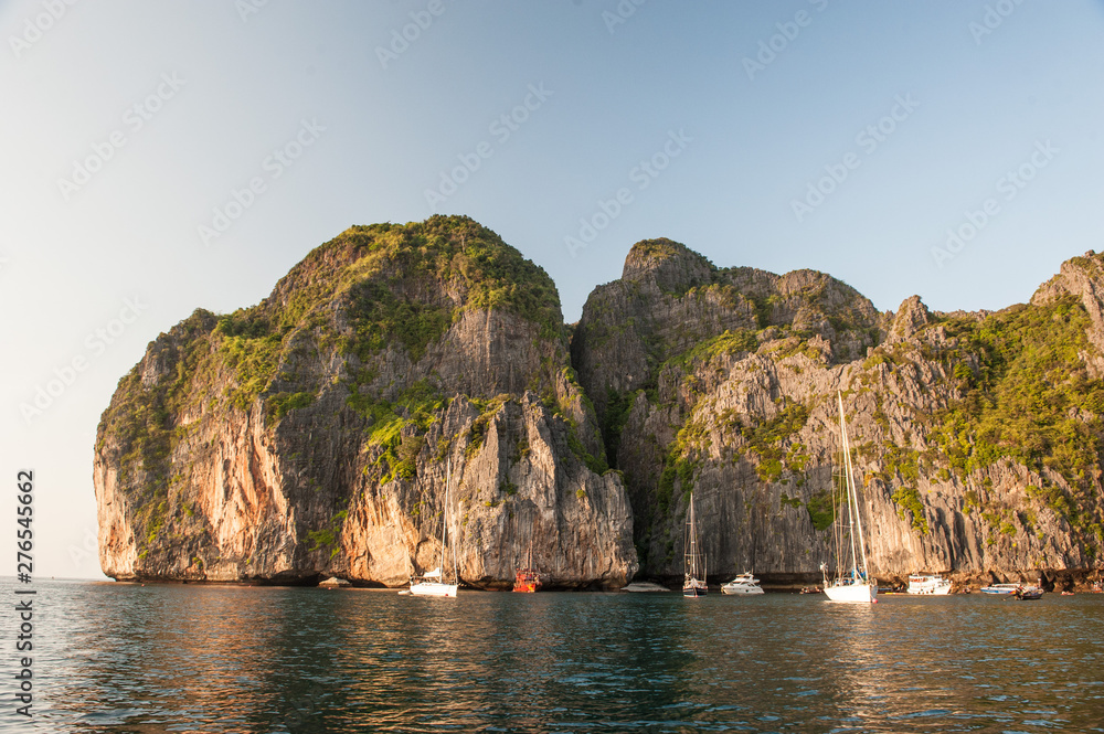 Traditional long tail boats, tourists, rocks and sea on and around Maya Bay beach in Koh Phi Phi Island, Krabi, Southern Thailand.