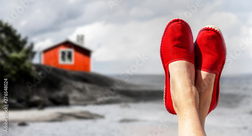 Beine mit roten Stoffschuhen vor Strand und Meer