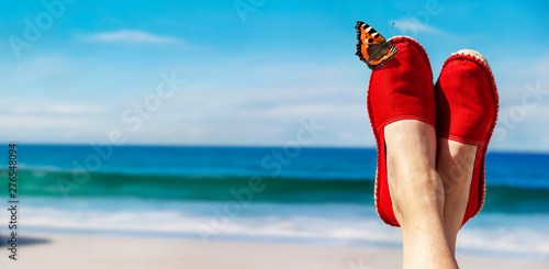 Beine mit roten Stoffschuhen vor Strand und Meer photo