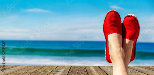 Beine mit roten Stoffschuhen vor Strand und Meer