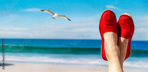 Beine mit roten Stoffschuhen vor Strand und Meer