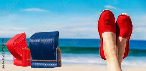 Beine mit roten Stoffschuhen vor Strand und Meer