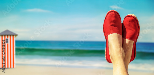 Beine mit roten Stoffschuhen vor Strand und Meer