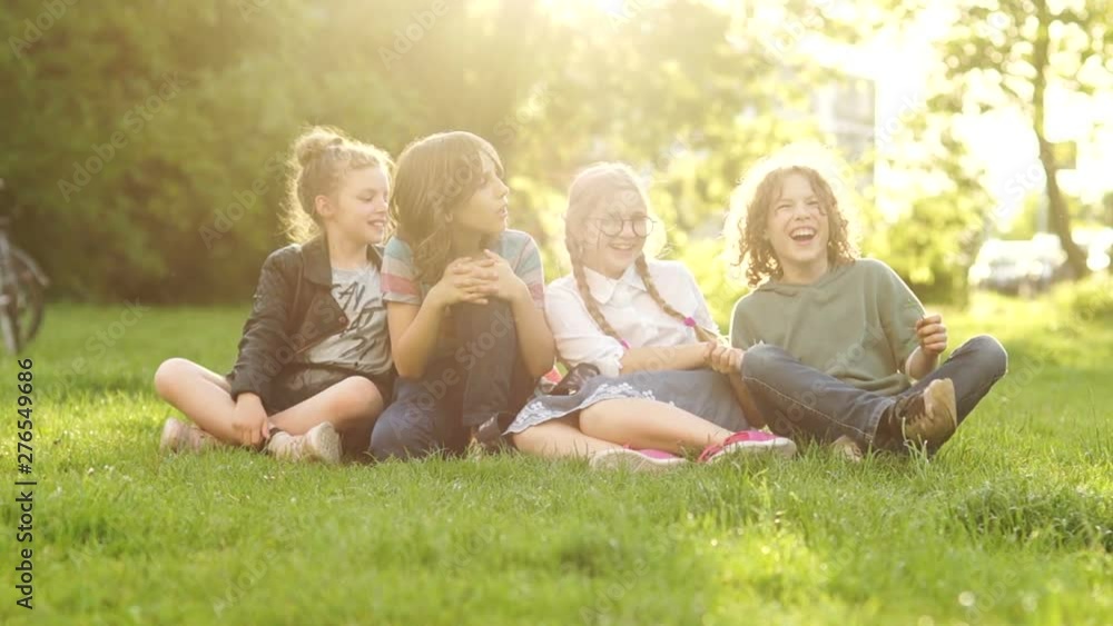 Beautiful schoolchildren, boys and girls laugh sitting on the grass during a school break. Back to school, a group of teenagers on a picnic. Sunset sun rays Beautiful schoolchildren, boys and girls laugh sitting on the grass during a school break. Back to school, a group of teenagers on a picnic. Sunset sun rays