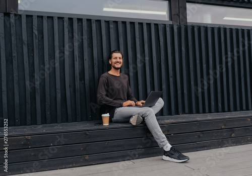 Freelancer Man siting in urban city with a laptop phone camera and coffee or tea with misic headphones