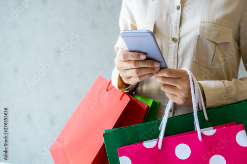 Closeup of woman holding shopping bags and using smartphone. Shopping online concept