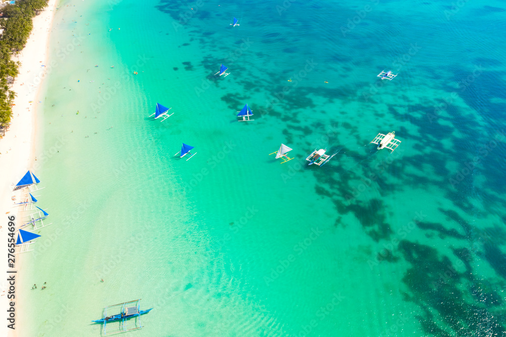 Obraz premium Blue sailing boats off the island of Boracay. Seascape, beautiful lagoon and white beach. Resort of the Philippines, top view.