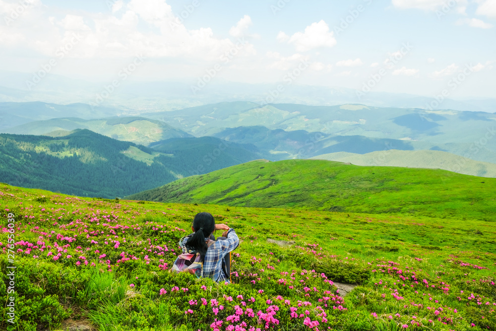 Happy woman 59 years old sits among the flowers of Rhododendron in the Alpine meadows in the Carpathians mountains. Ukrainian tourism. View from the back. Self-isolation concept.