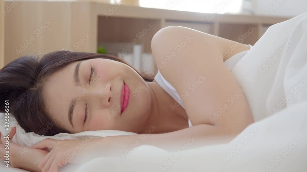 Asian woman smiling lying on bed in bedroom, Beautiful japanese female using relax time after wake up at home. Lifestyle women using relax time at home concept. Slow motion shot.