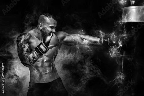 Sportsman man boxer fighting in gloves with boxing punching bag on dark background with smoke. Copy Space. Black and white photo.