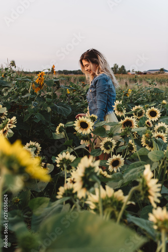 A women in her twenties with blonde hair exploring a sunflower field at sunset