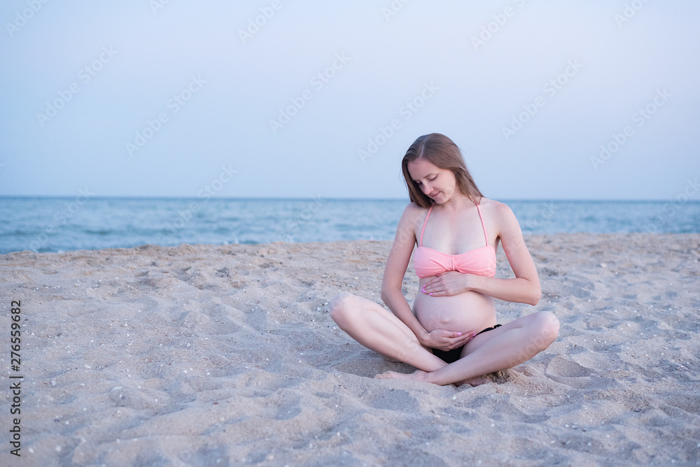 Pregnant woman sits on the beach and enjoys. Soft evening light, deserted beach. Pregnant woman sits on the beach and enjoys. Soft evening light, deserted beach.