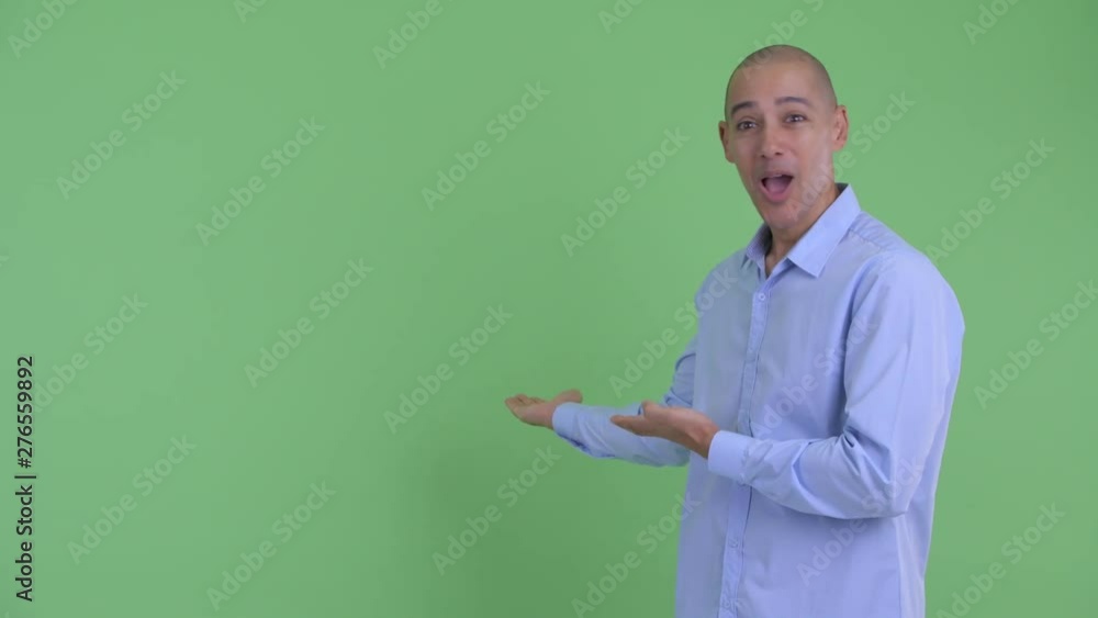 Happy bald multi ethnic businessman showing to back and looking surprised Happy bald multi ethnic businessman showing to back and looking surprised