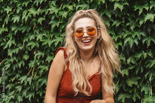 A beautiful woman in her twenties wearing 70s style clothing and sunglasses posing for portraits and smiling 