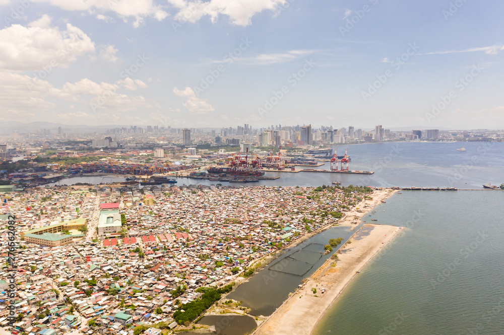 Port in Manila, Philippines. Sea port with cargo cranes. Cityscape with poor areas and business center in the distance, view from above. Asian metropolis.