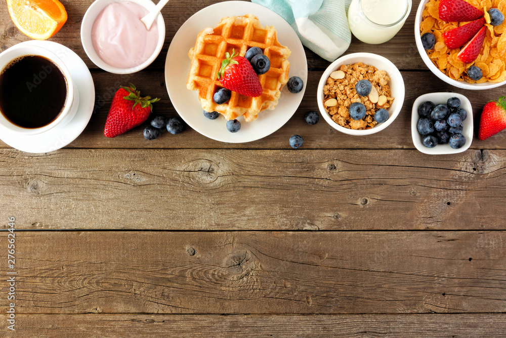 Breakfast food top border. Fruits, cereal, waffles, yogurt and coffee. Top view over a dark wood background with copy space. Breakfast food top border. Fruits, cereal, waffles, yogurt and coffee. Top view over a dark wood background with copy space.