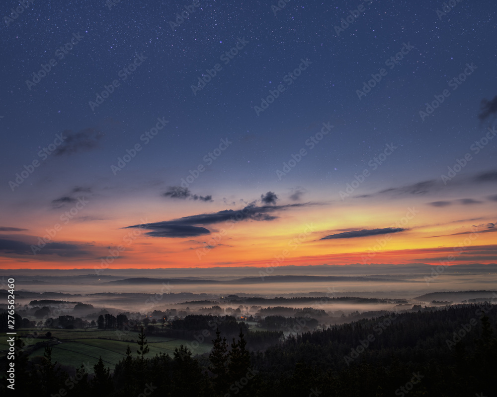 Naklejka premium Starry dawn over a misty landscape