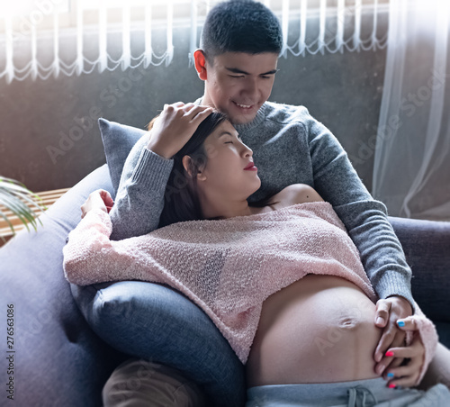 The pregnant woman laying down on sofa and hugging by her husband,put hand touch belly,waith for newborn,with love and care,vintage and art tone,blurry light around