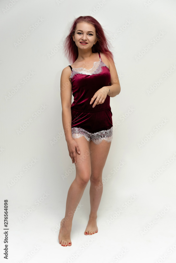 Concept portrait of a full-length pretty sexy girl with purple hair in beautiful red lingerie on a white background. She smiles, happy with life, happy. Hair flying, front view. Made in a studio.