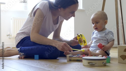 Mother With 8 Month Old Baby Boy Playing With Musical Instruments At Home   