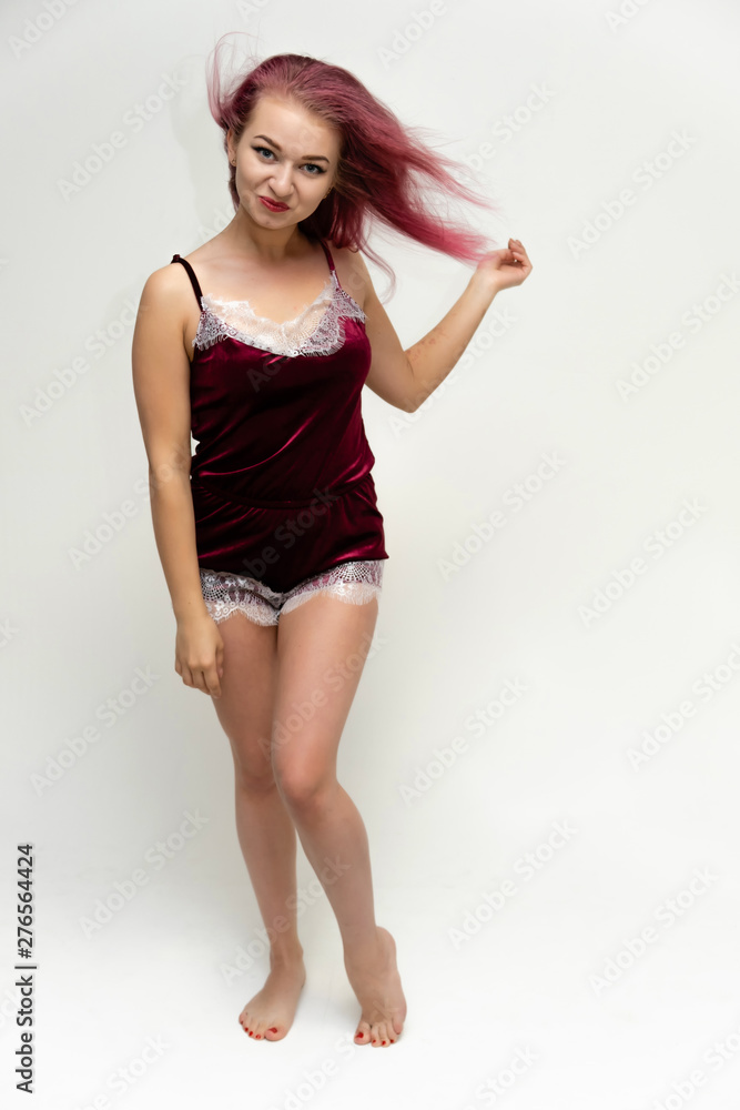 Concept portrait of a full-length pretty sexy girl with purple hair in beautiful red lingerie on a white background. She smiles, happy with life, happy. Hair flying, front view. Made in a studio.