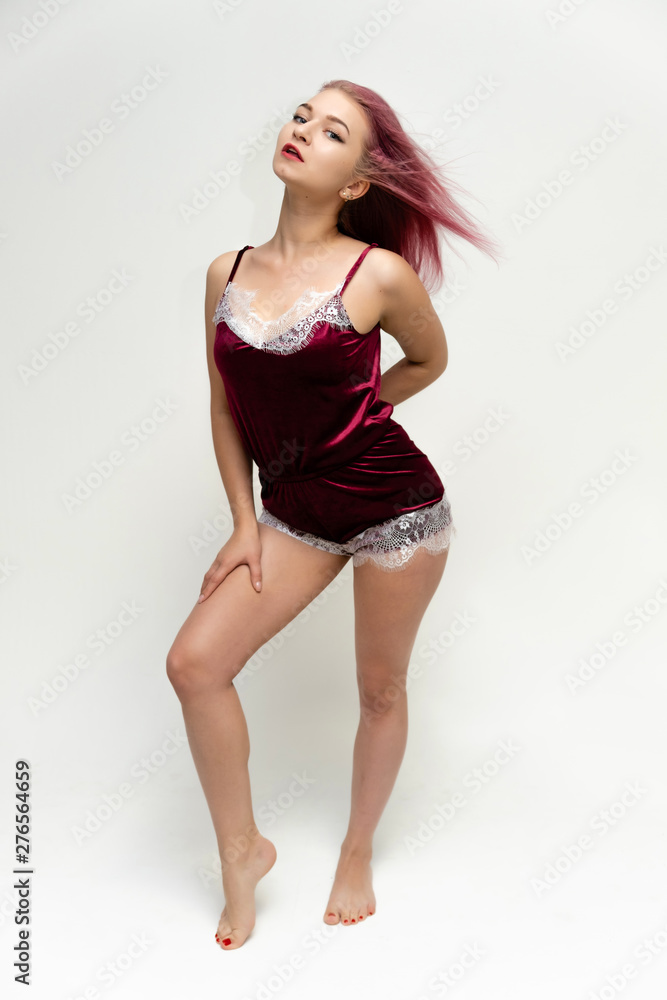 Concept portrait of a full-length pretty sexy girl with purple hair in beautiful red lingerie on a white background. She smiles, happy with life, happy. Hair flying, front view. Made in a studio.