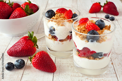 Strawberry and blueberry parfaits in glasses against a bright white wood background