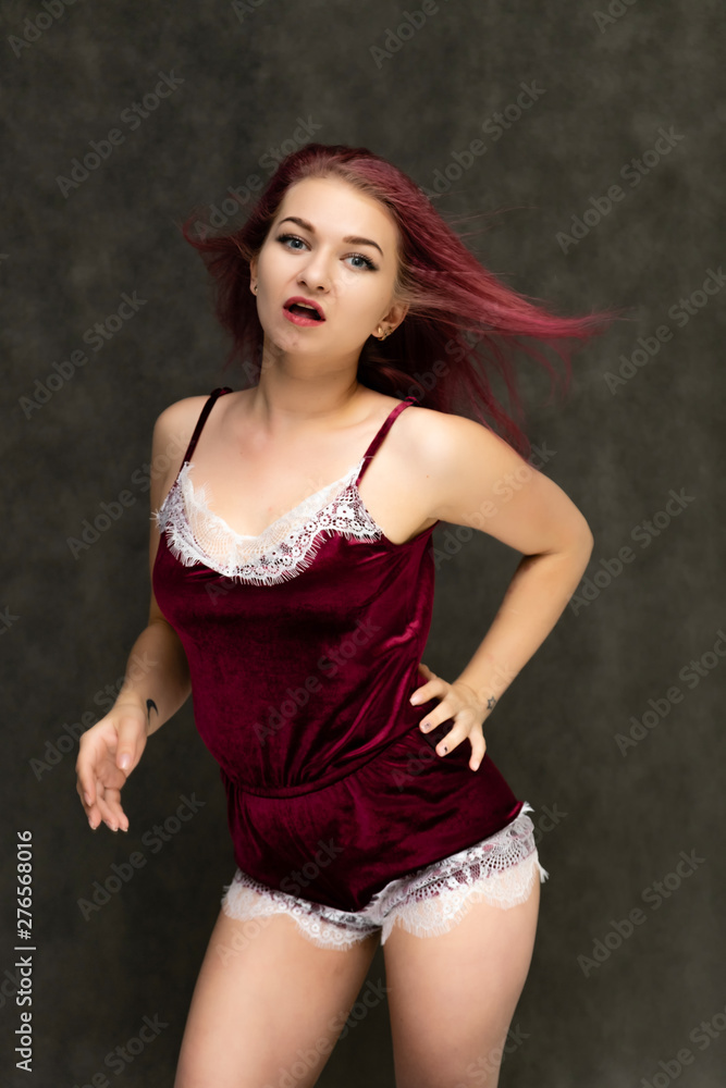 Concept portrait of a knee-high pretty sexy girl with purple hair in beautiful red lingerie on a gray background. She smiles, happy with life, happy. Hair flying, front view. Made in a studio. Concept portrait of a knee-high pretty sexy girl with purple hair in beautiful red lingerie on a gray background. She smiles, happy with life, happy. Hair flying, front view. Made in a studio.