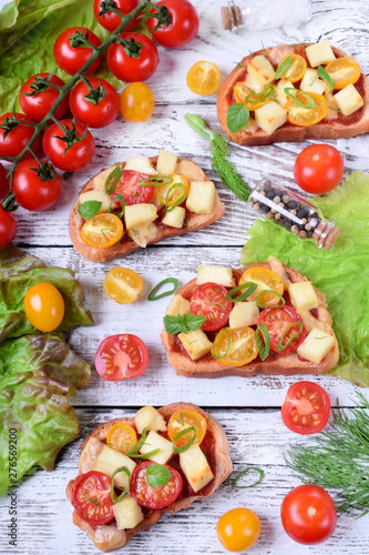 Bruschetta with cherry tomatoes and cheese topped with greenery on the white wooden table