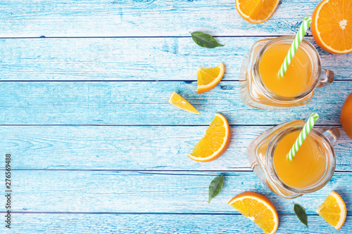Orange juice in glass jars and fresh oranges on a blue background.