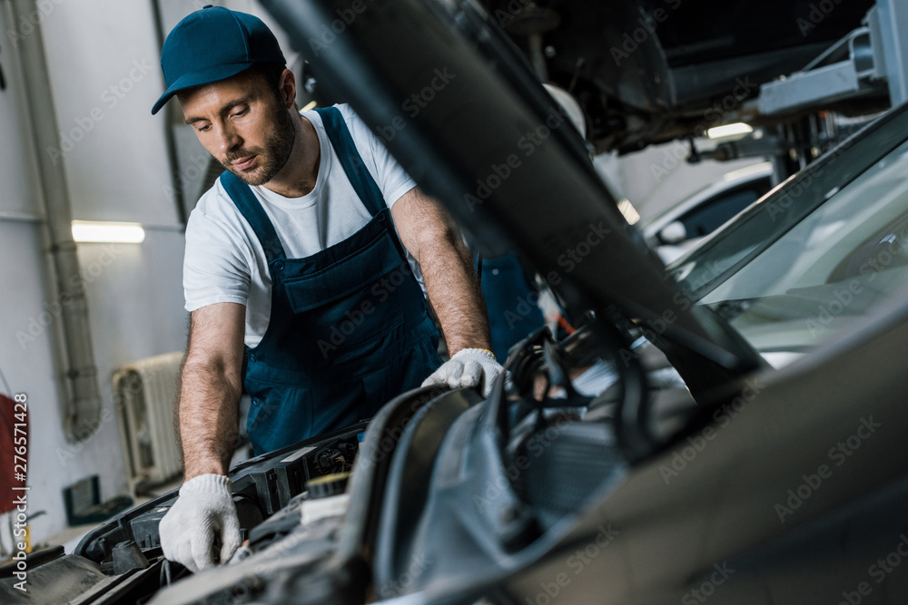 selective focus of handsome car mechanic in gloves looking at car engine selective focus of handsome car mechanic in gloves looking at car engine