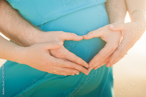 Male and female hands hold a pregnant belly closeup and copy space. Pregnant in a blue dress and men's hands with a heart