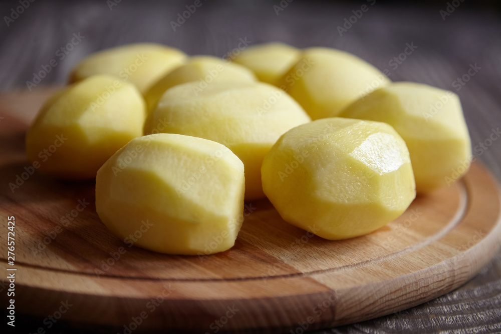 Peeled potatoes on wooden cutting board on brown table. Cooking food from natural products. Root vegetable. Raw ingredient: uncooked whole potatoes Peeled potatoes on wooden cutting board on brown table. Cooking food from natural products. Root vegetable. Raw ingredient: uncooked whole potatoes