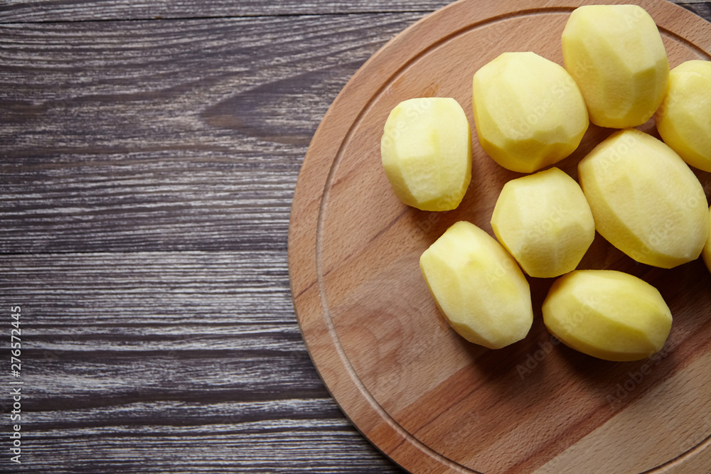 Peeled potatoes on wooden cutting board on brown table. Cooking food from natural products. Root vegetable. Raw ingredient: uncooked whole potatoes Peeled potatoes on wooden cutting board on brown table. Cooking food from natural products. Root vegetable. Raw ingredient: uncooked whole potatoes