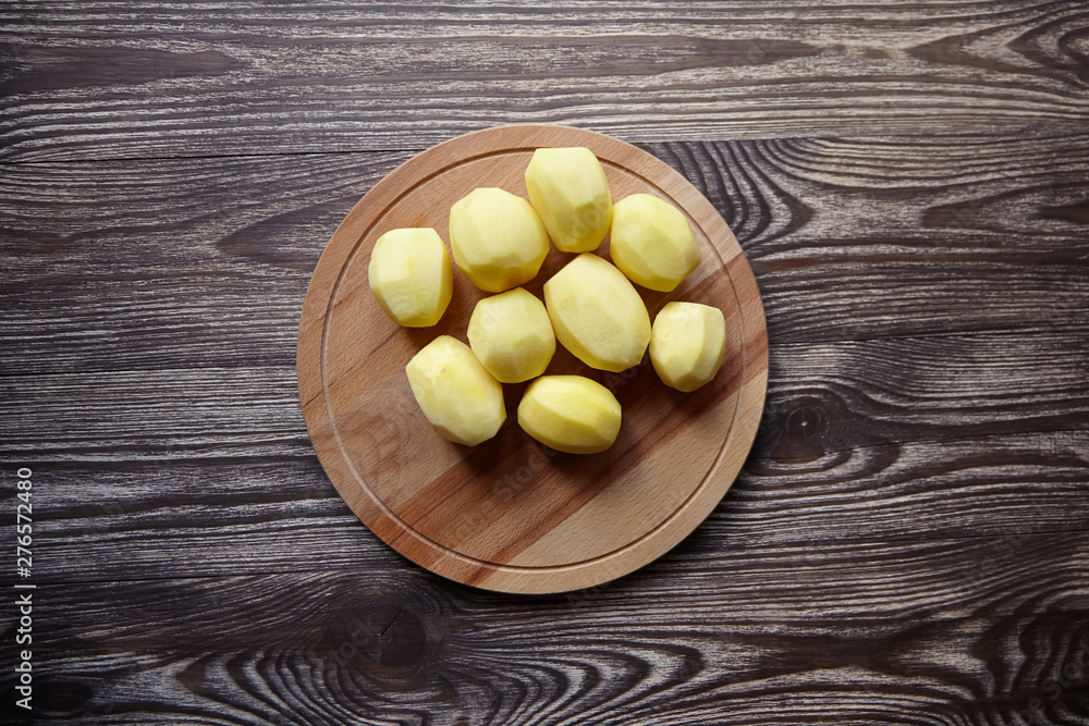 Peeled potatoes on wooden cutting board on brown table. Cooking food from natural products. Root vegetable. Raw ingredient: uncooked whole potatoes Peeled potatoes on wooden cutting board on brown table. Cooking food from natural products. Root vegetable. Raw ingredient: uncooked whole potatoes