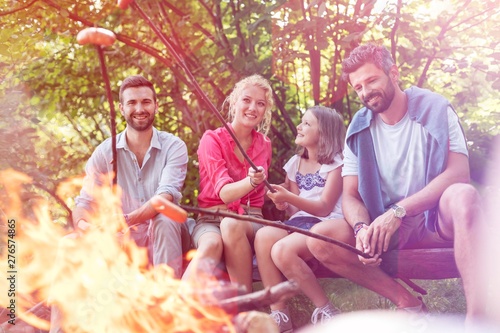 Happy family with male friend roasting sausages over campfire at park © moodboard