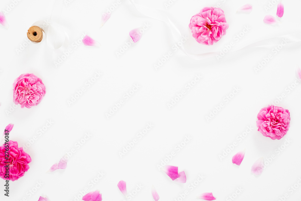 Minimal flat lay style composition with empty space in the center made of blooming pink flowers. Top view floral decorative frame with pink rose and ribbon on white background.