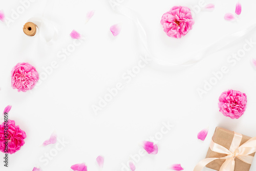 Minimal flat lay style composition with empty space in the center made of blooming pink flowers. Top view floral decorative frame with pink rose, ribbon and gift box on white background.