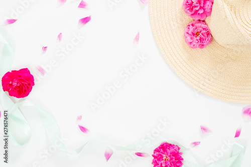 Minimal style composition with beach straw hat, pink rose flowers bud and petal and blue mint ribbon on white background. Flat lay, top view still life concept.