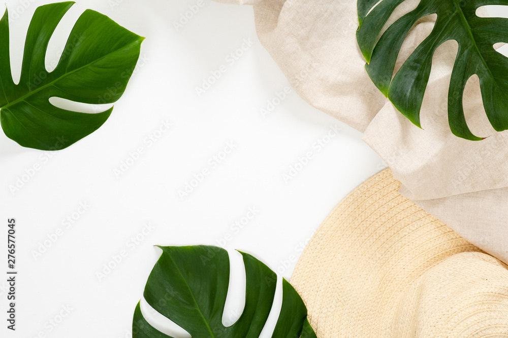 Summer vacation concept with tropical monstera leaves and straw hat on white background. Minimal flat lay style composition with copy space. Top view, overhead. - obrazy, fototapety, plakaty 