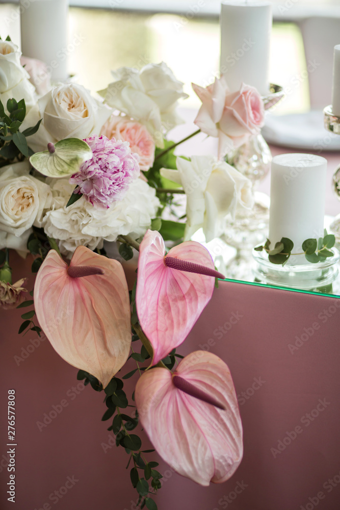 Fototapeta premium The wedding table setting for the newlyweds is decorated with fresh flowers of carnation, rose, anthurium and eucalyptus leaves. Silver candlesticks, white candles. Wedding floristry. Close-up details