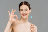 cheerful naked woman holding toothbrush while showing ok sign isolated on grey