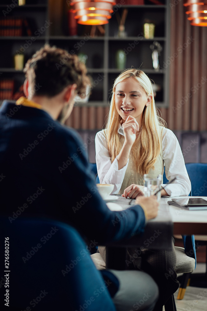 Φωτογραφία Smiling Caucasian blonde businesswoman dressed smart casual discussing with her male colleague about project while sitting in coffe shop