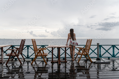 A young girl in a dress is standing in a sea restaurant. The island has rainy weather