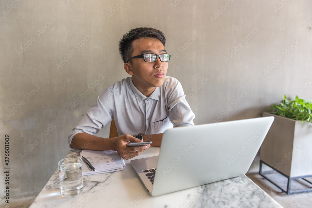 Young man using cellphone and laptop and thinking at office Young man using cellphone and laptop and thinking at office