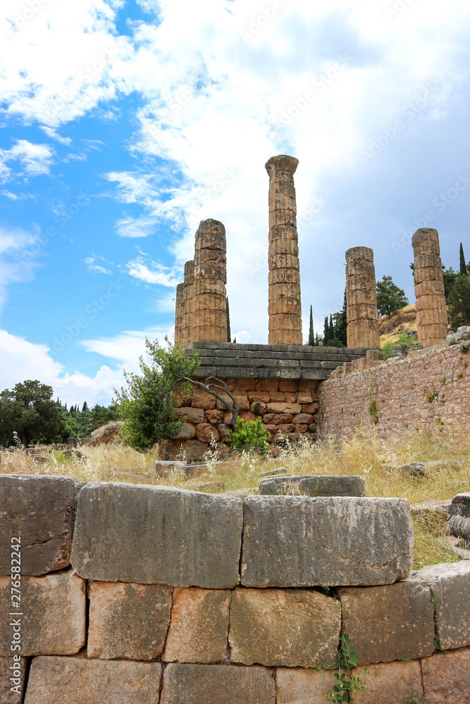 fragments of polygonal wall and ruins of ancient greek temple of apollo with columns, Delphi, Greece with blue sky and clouds on the background