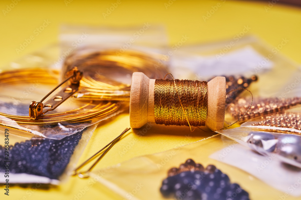 Embroidery products and tools. The spool of metallic thread, Japanese seed beads and sequins on a yellow background Embroidery products and tools. The spool of metallic thread, Japanese seed beads and sequins on a yellow background