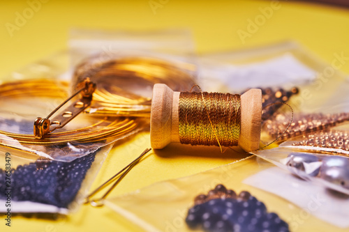 Embroidery products and tools. The spool of metallic thread, Japanese seed beads and sequins on a yellow background